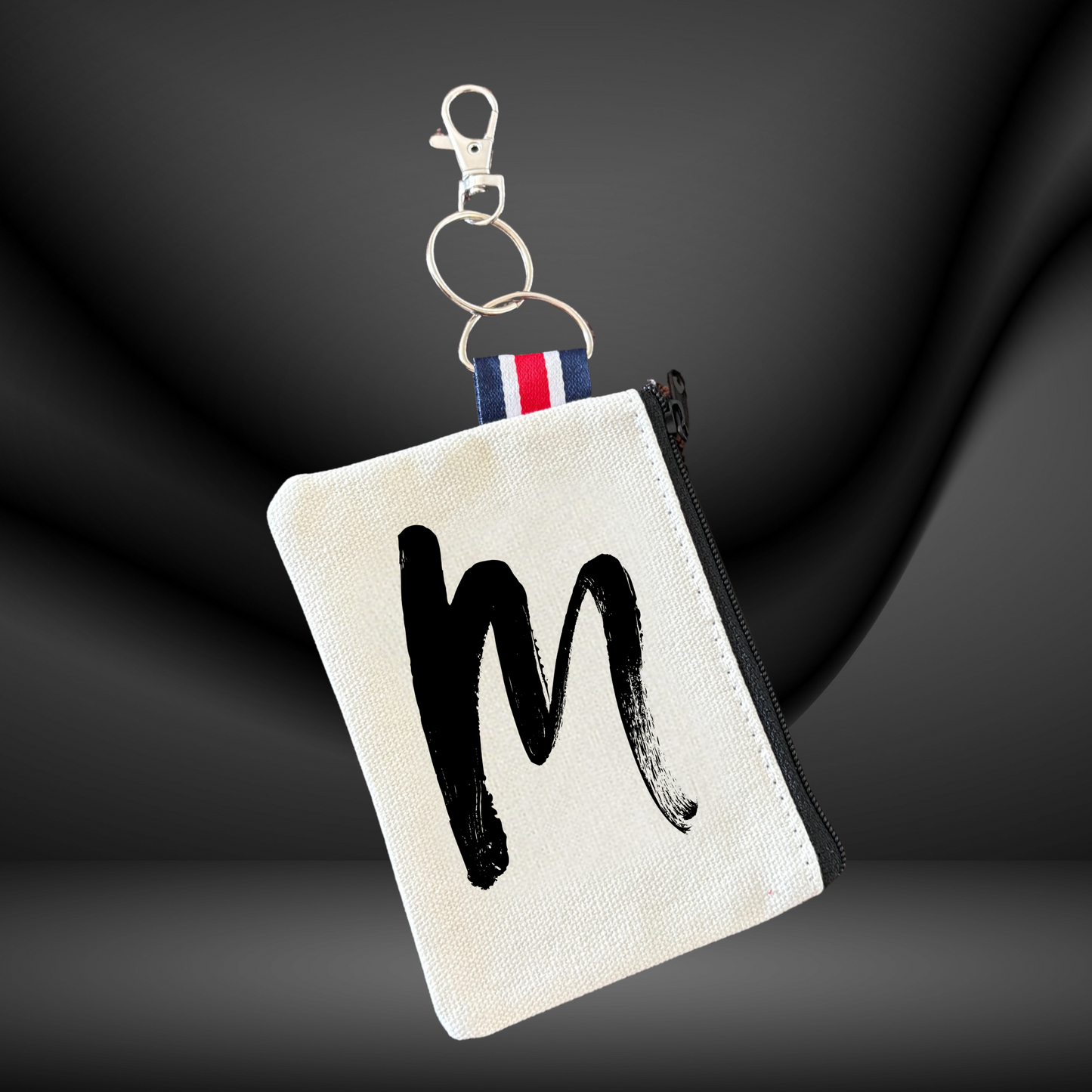 Canvas zip pouch keychain with a black initial 'm' photographed on a dark background
