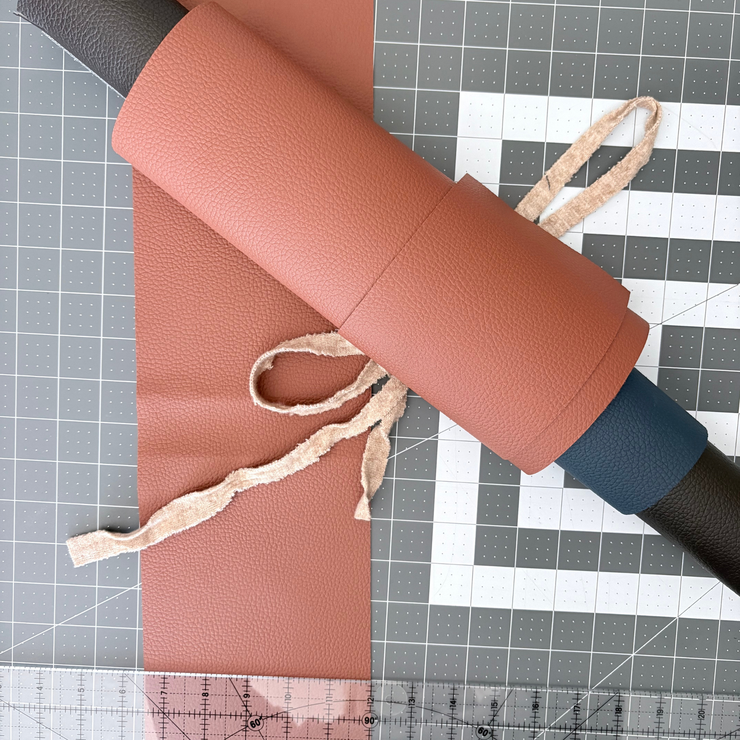 Roll of tan, nvy and black vegan leather on a cutting mat with grid lines