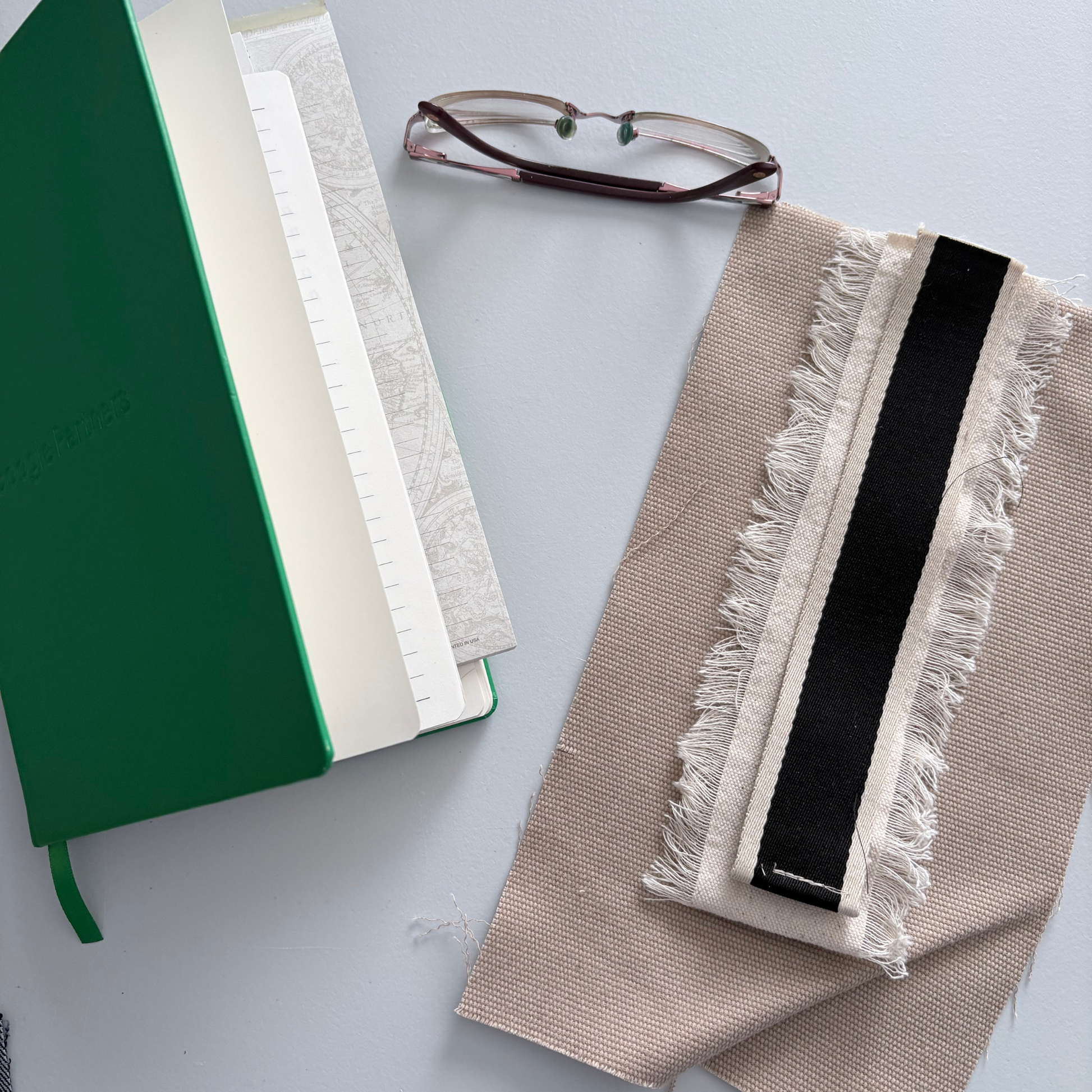 Green notebook, white book, and beige canvas with black stripe on a light gray surface.