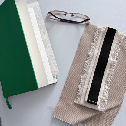 Green notebook, white book, and beige canvas with black stripe on a light gray surface.