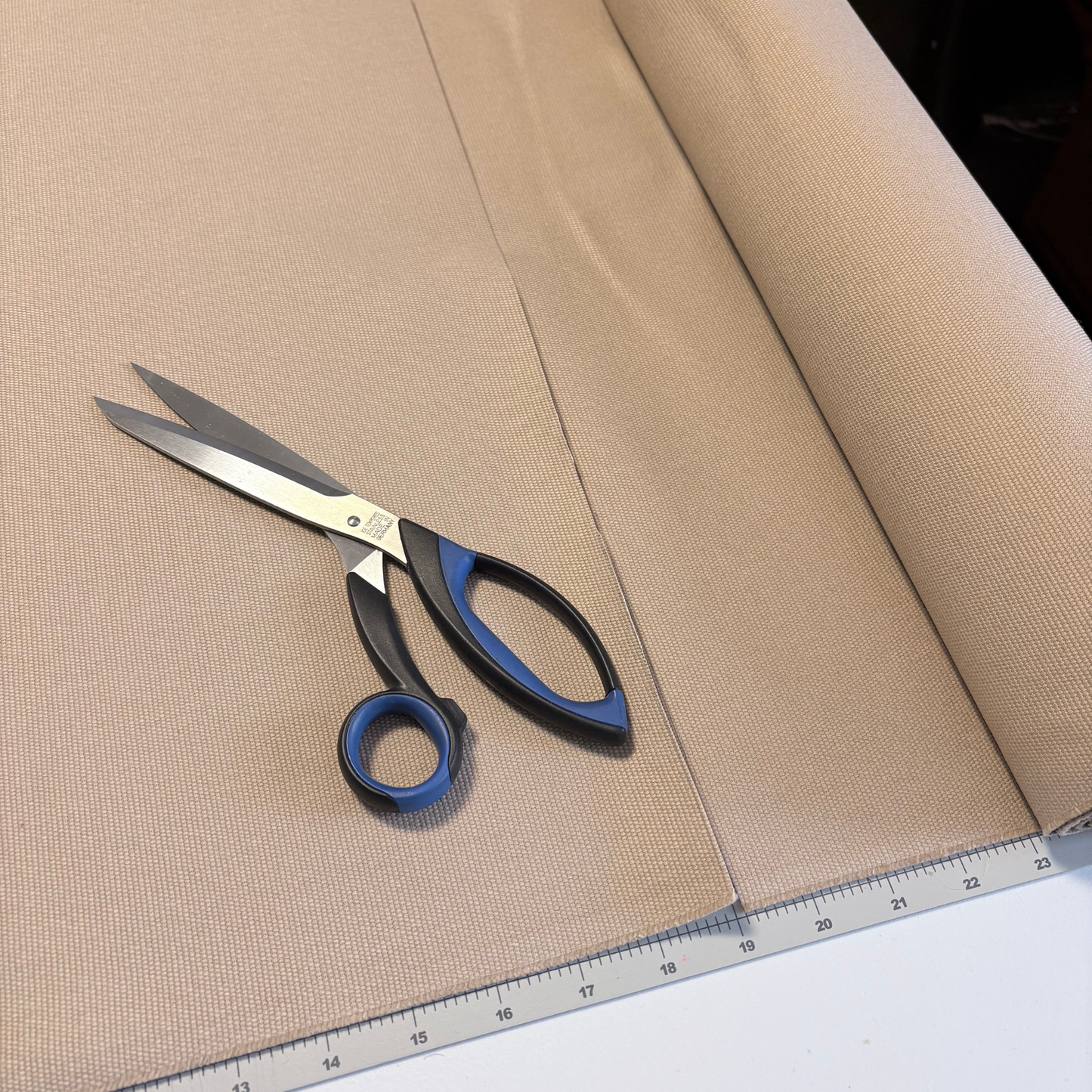 Roll of beige fabric with a pair of scissors and a ruler on a white surface